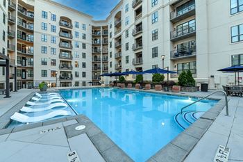 an outdoor swimming pool with lounge chairs and umbrellas in front of an apartment building